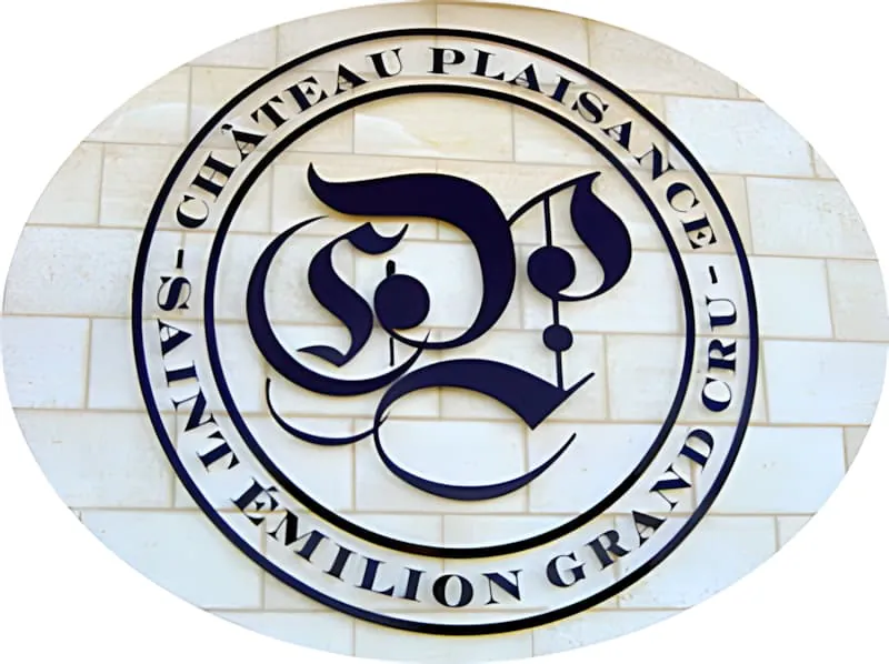 安装在白色石墙上的圆形金属标识,以哥特式字体装饰「CP」首字母,边框有「Château Plaisance」和「Saint-Émilion Grand Cru」文字。
