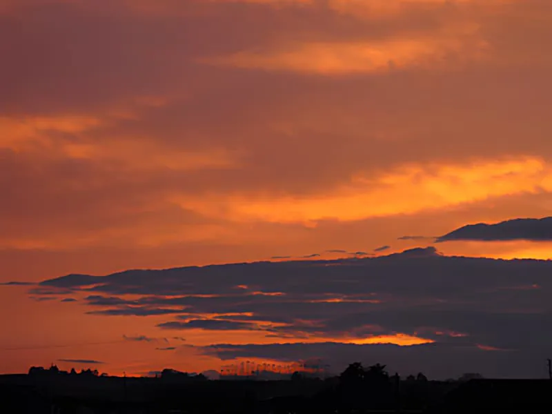 Ein dramatischer Sonnenuntergang mit lebendigen orange und roten Wolken, die sich über den Himmel über eine silhouettierte Landschaft erstrecken.