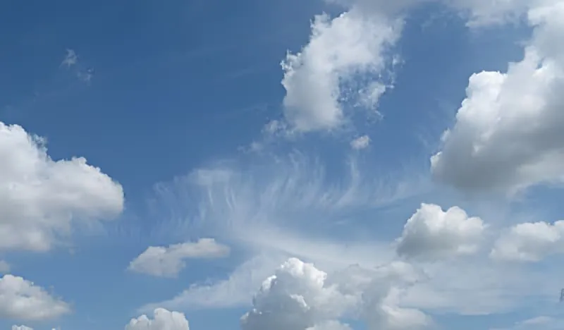 A bright blue sky filled with white puffy clouds, representing ideal weather conditions for vineyard work.