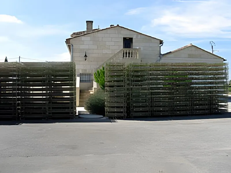Piles de caisses métalliques grillagées devant un bâtiment en pierre, utilisées pour stocker et transporter les bouteilles de vin pendant le processus de mise en bouteille.