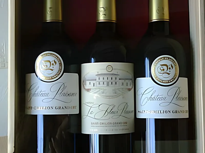 Trois bouteilles de vin foncées avec des étiquettes blanches et dorées montrant la marque « Château Plaisance Saint-Émilion Grand Cru ».