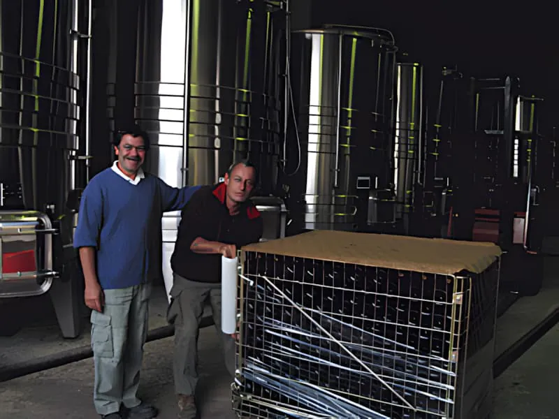 Un ouvrier de vignoble, souriant, charge des bouteilles de vin vides dans des cages métalliques sur un tapis roulant au Château Plaisance.